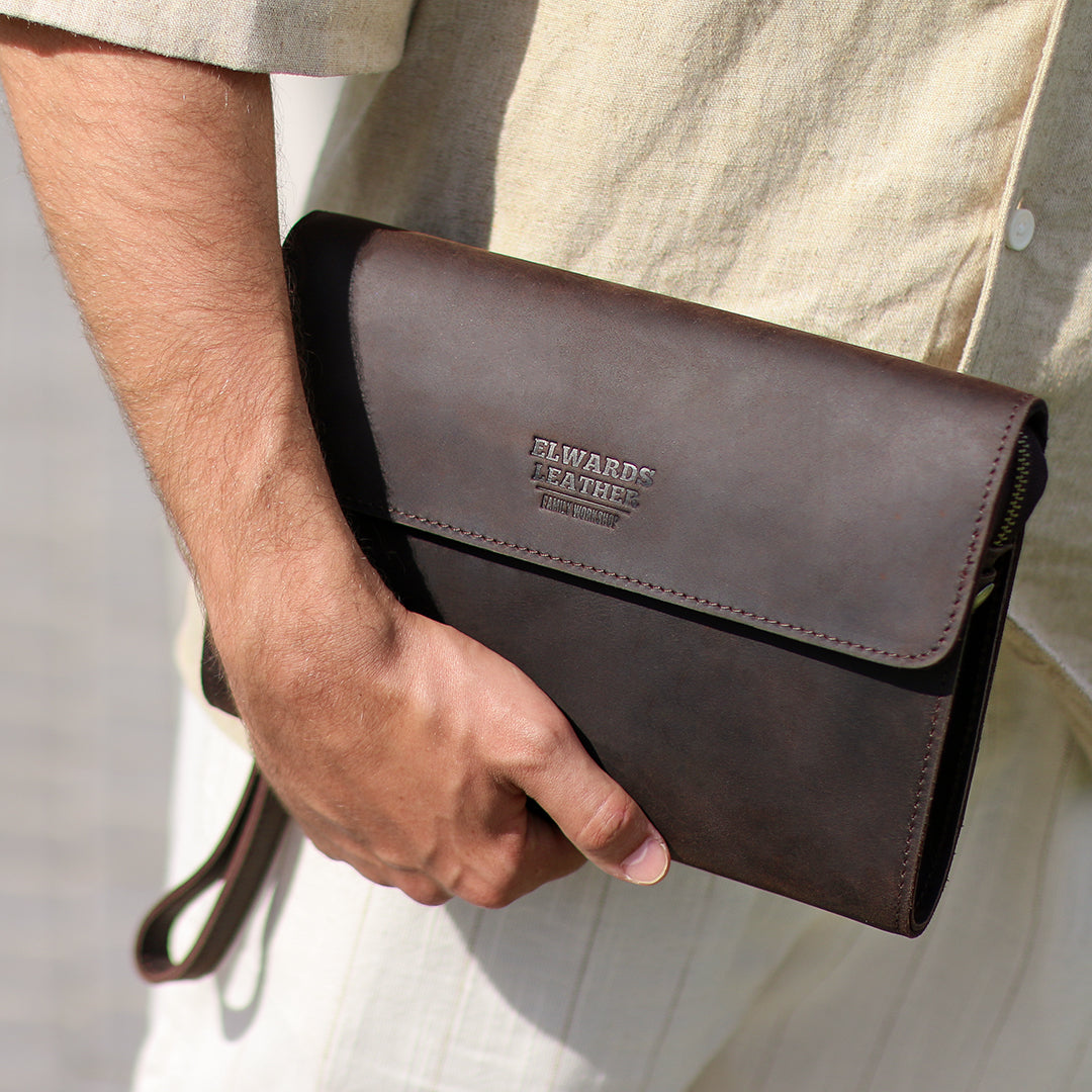 Men&#39;s dark brown leather clutch being tucked under the arm, showcasing its sleek and portable design for casual outings.