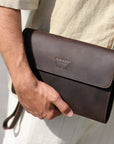 Men's dark brown leather clutch being tucked under the arm, showcasing its sleek and portable design for casual outings.