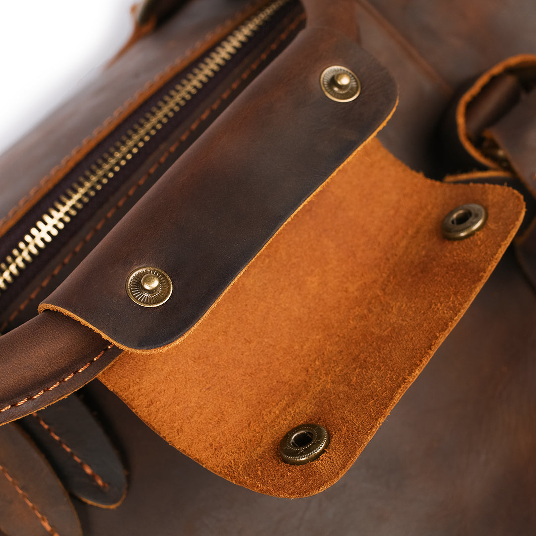 Close-up of magnetic snaps and brass details on handcrafted brown leather duffle bag.