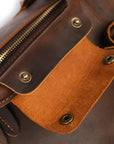 Close-up of magnetic snaps and brass details on handcrafted brown leather duffle bag.