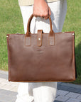 Man holding a luxury brown leather work bag with reinforced handles, showcasing its professional and vintage design.