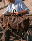 Man sitting outdoors with vintage handmade weekender bag, emphasizing its durable crazy horse leather and timeless style.