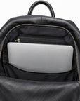 Black leather backpack shown open, displaying a silver laptop in the front pocket and a black zippered interior compartment, on a white background.