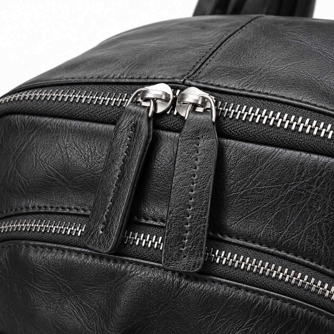 Close-up of a black textured leather bag with dual silver-tone zippers and pull tabs on a white background.