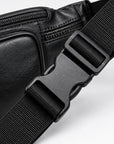 Close-up of a black leather crossbody bag with a matching black adjustable webbing strap and plastic quick-release buckle on a white background.
