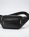 A black genuine leather waist bag with multiple zippered compartments and an adjustable black webbing strap, shown on a light gray studio background.