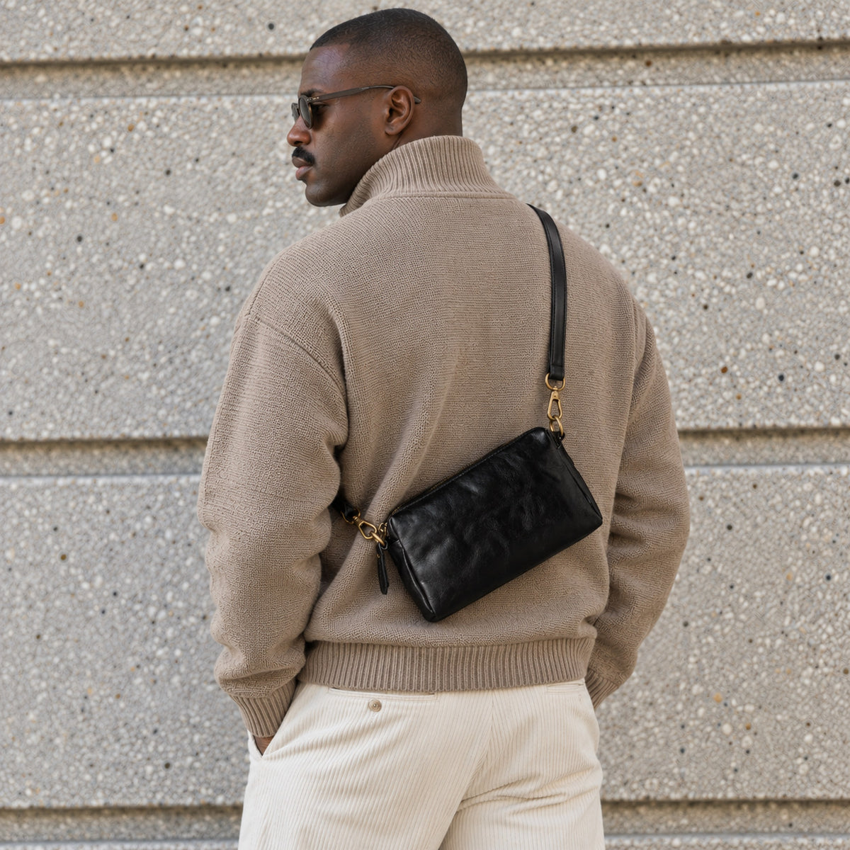 Back view of a man wearing a black leather crossbody bag with gold-tone hardware