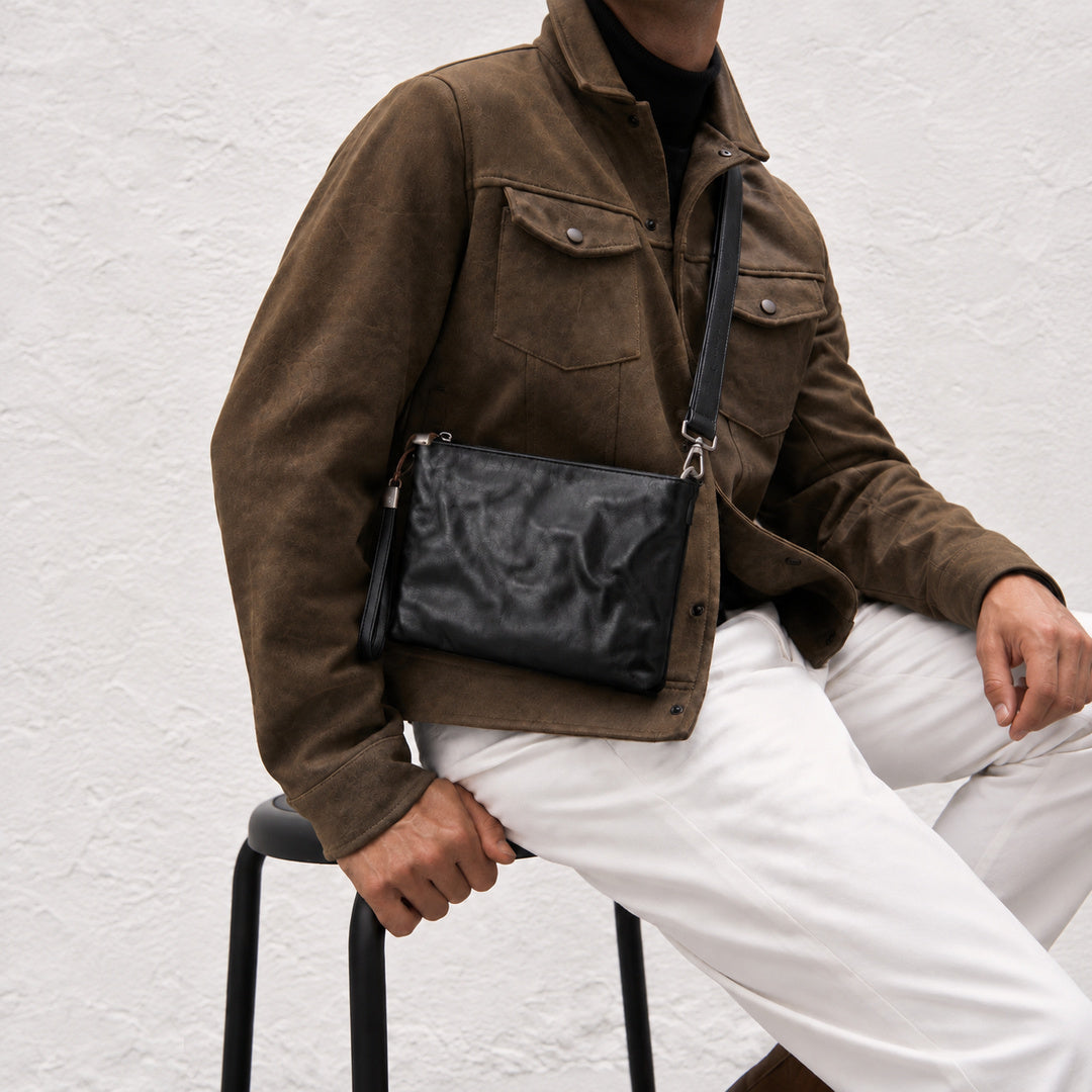 Close-up of a textured black leather crossbody bag with detachable shoulder strap and wrist strap