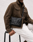 Close-up of a textured black leather crossbody bag with detachable shoulder strap and wrist strap