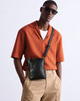 Man wearing a black leather crossbody bag with an adjustable shoulder strap