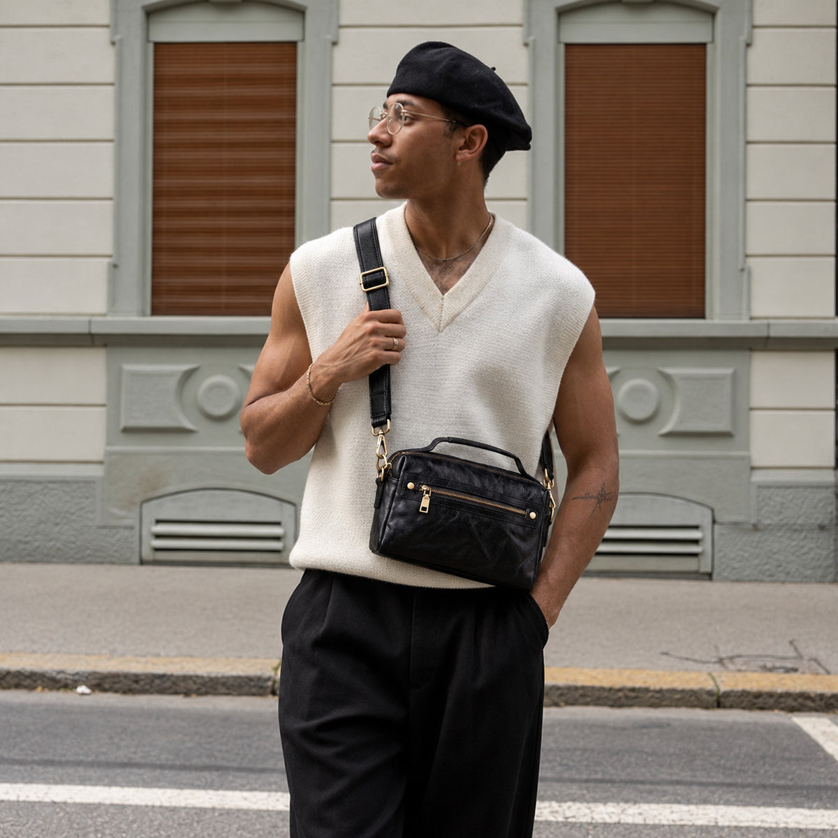 Man wearing a black leather crossbody bag with top handle, adjustable shoulder strap and gold-tone hardware.