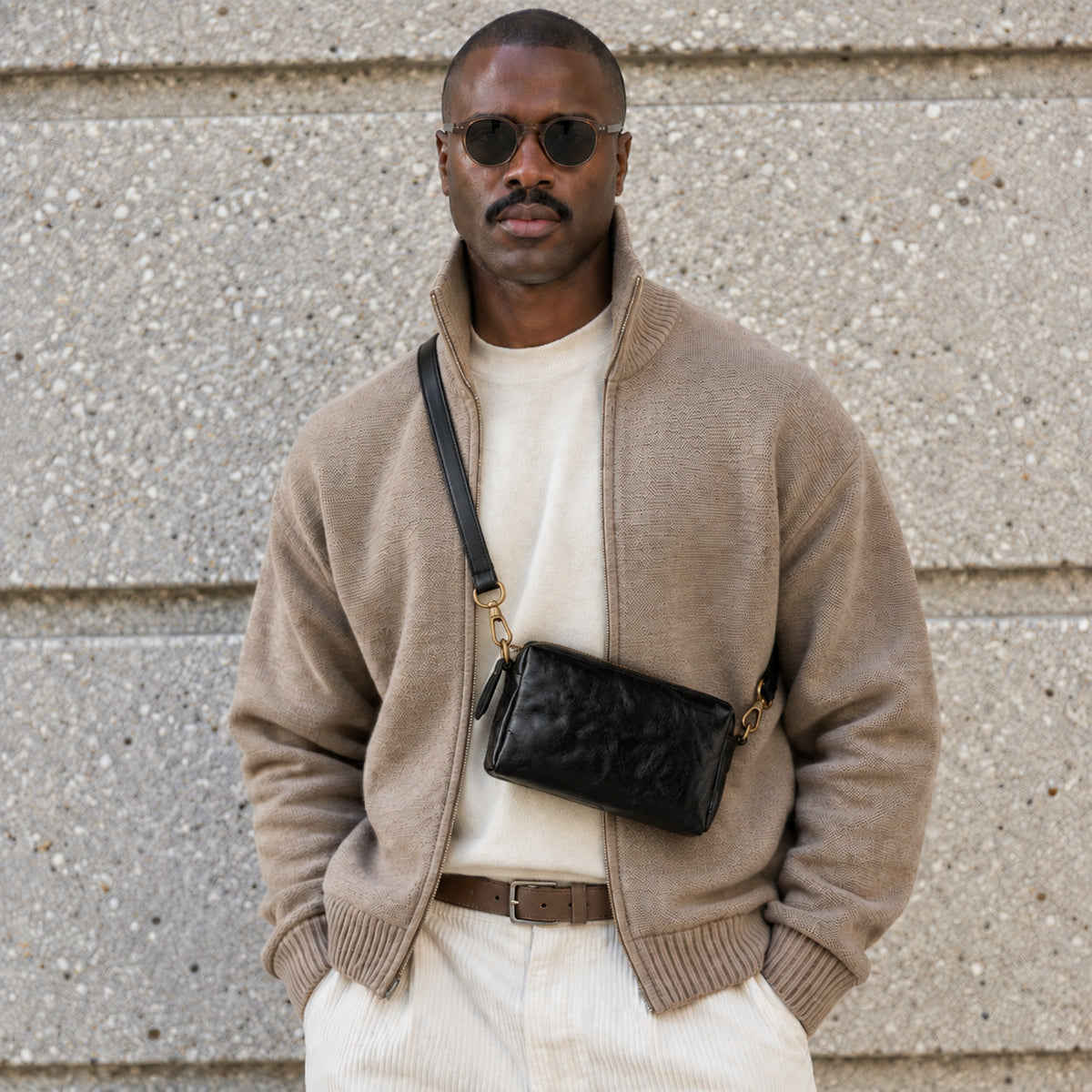 Man wearing a black leather crossbody bag with gold-tone hardware and adjustable strap