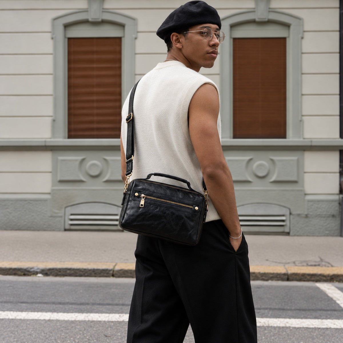 Man wearing a black leather crossbody bag at the hip, featuring a top handle, front zip pocket and adjustable strap.