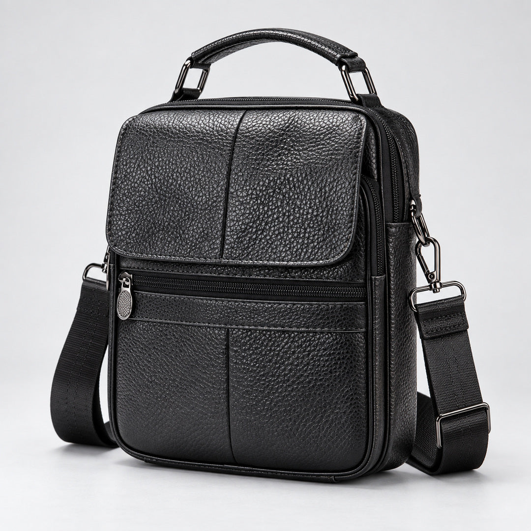 Black pebbled leather crossbody bag with a top handle, front zip pocket, and adjustable shoulder strap, photographed on a light gray studio background.