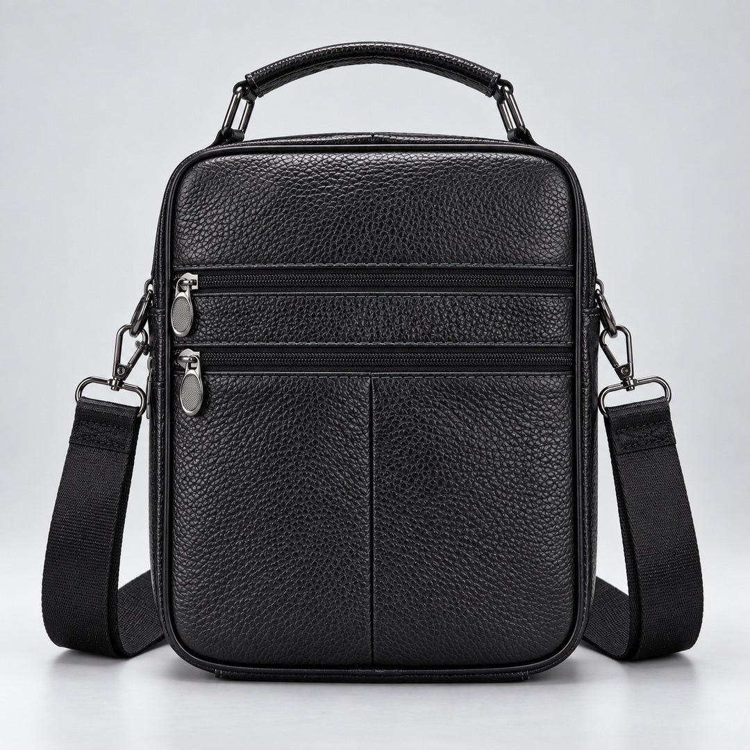Black pebbled leather crossbody bag with a top handle, front zippered pockets, and an adjustable shoulder strap, shown on a light gray studio background.