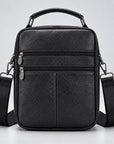 Black pebbled leather crossbody bag with a top handle, front zippered pockets, and an adjustable shoulder strap, shown on a light gray studio background.