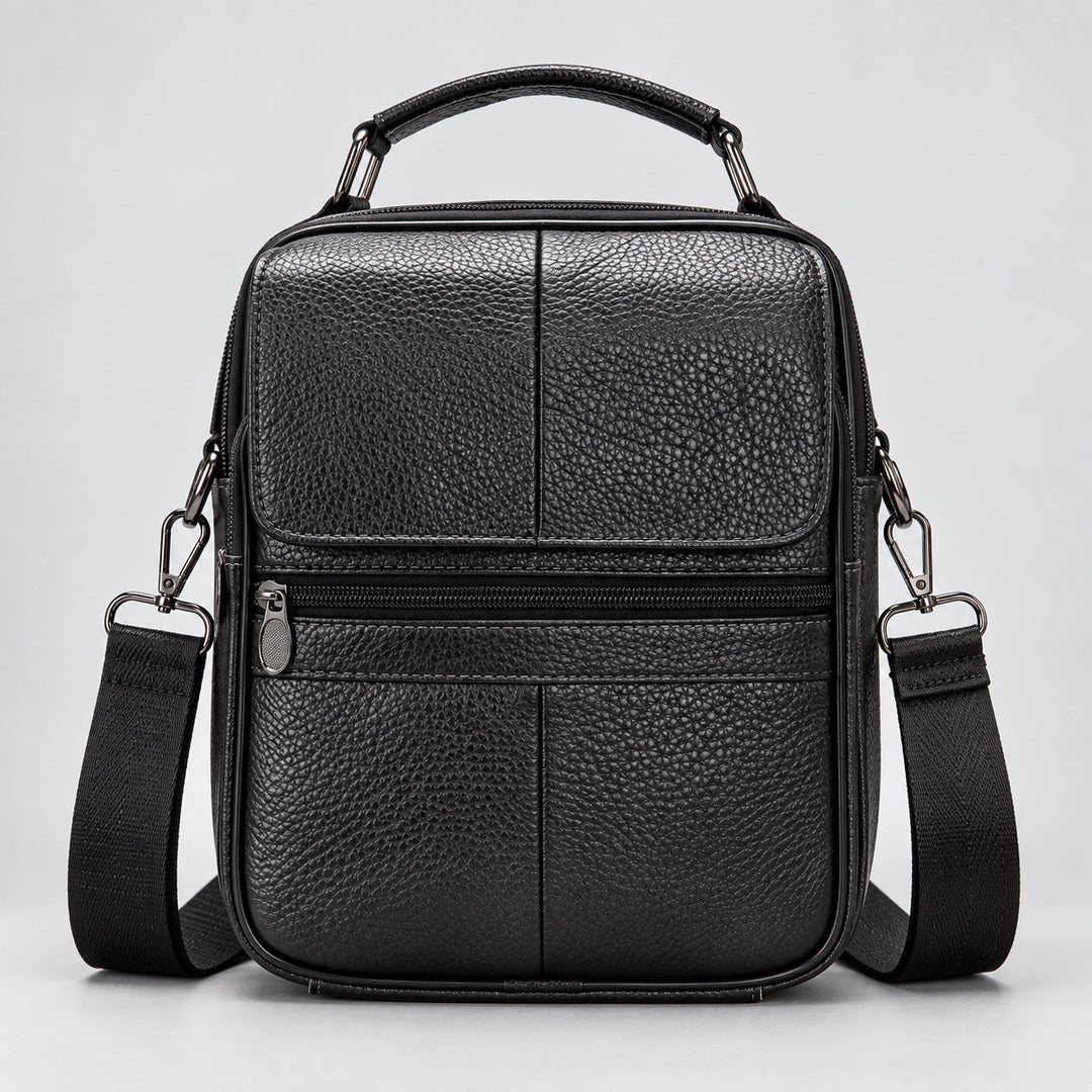 A black pebbled leather crossbody bag with a top handle, front zip pocket, and adjustable shoulder strap, shown against a light gray background.