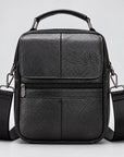 A black pebbled leather crossbody bag with a top handle, front zip pocket, and adjustable shoulder strap, shown against a light gray background.