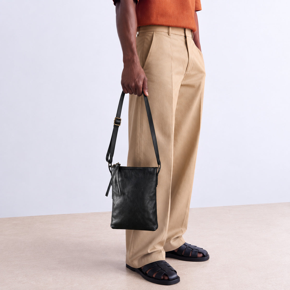 Man carrying a black leather shoulder bag by its adjustable strap