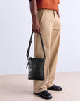 Man carrying a black leather shoulder bag by its adjustable strap