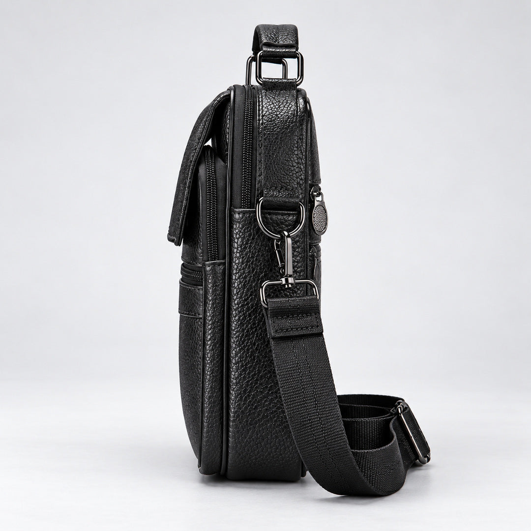 A black textured leather crossbody bag shown from a side profile view, featuring a matching black webbing strap with silver-tone metal hardware, set against a clean light gray background.