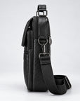 A black textured leather crossbody bag shown from a side profile view, featuring a matching black webbing strap with silver-tone metal hardware, set against a clean light gray background.