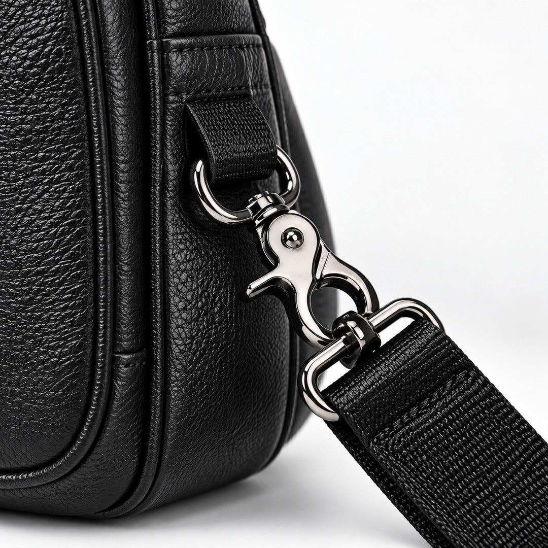 Close-up of a black pebbled leather bag with a silver metal clasp and a black webbed strap on a white background.