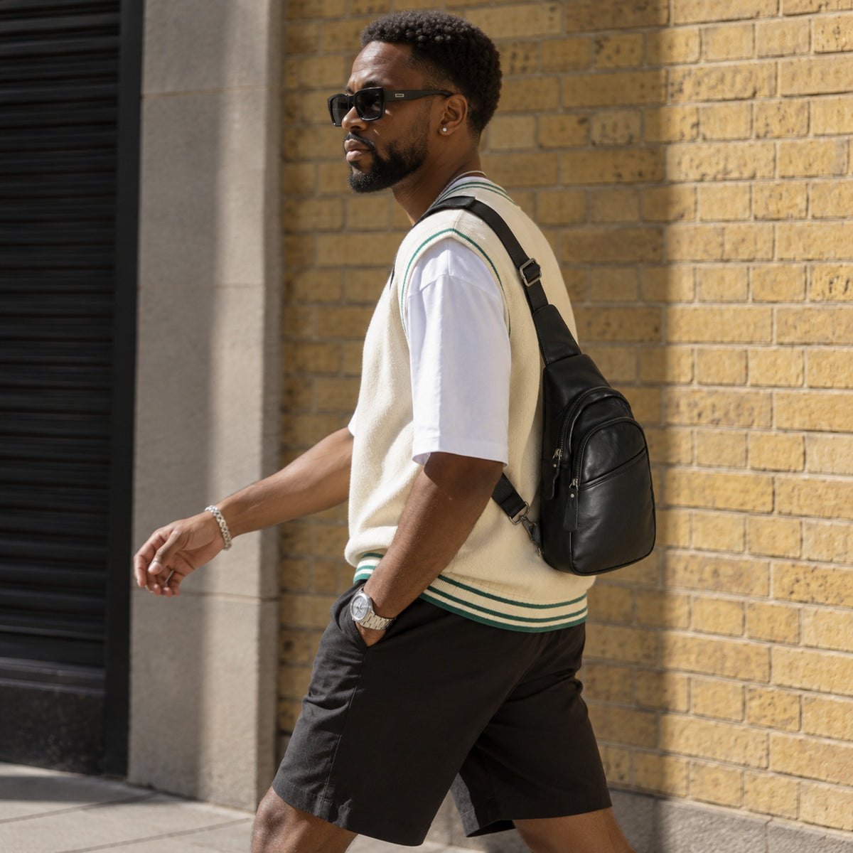 Side view of a man wearing a black leather sling bag with a casual summer outfit