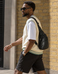 Side view of a man wearing a black leather sling bag with a casual summer outfit