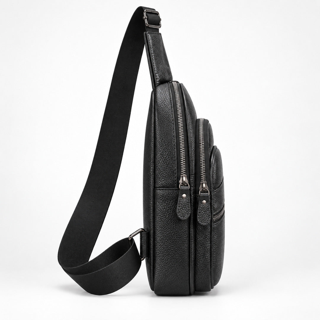 A black pebbled leather crossbody bag with a wide adjustable shoulder strap, shown from a side profile view against a clean white background.