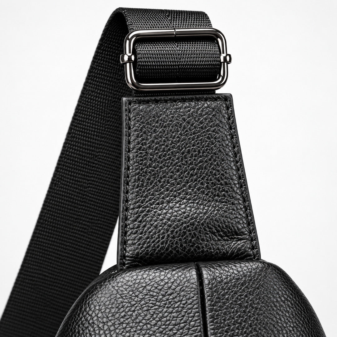 Close-up detail of a black pebbled leather bag strap with a silver-toned metal buckle and a black woven webbing strap on a light gray background.