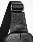 Close-up detail of a black pebbled leather bag strap with a silver-toned metal buckle and a black woven webbing strap on a light gray background.