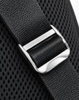 Close-up of a black woven strap with a polished silver metal buckle over a black mesh fabric background.