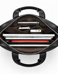 Top-down view of an open black leather laptop bag showing its interior organization with compartments holding a tablet, phone, power bank, and accessories, on a white background.