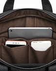 Close-up of the interior of a black textured bag showing a brown fabric organizer pocket holding a silver tablet, a white phone, and a rose gold phone.