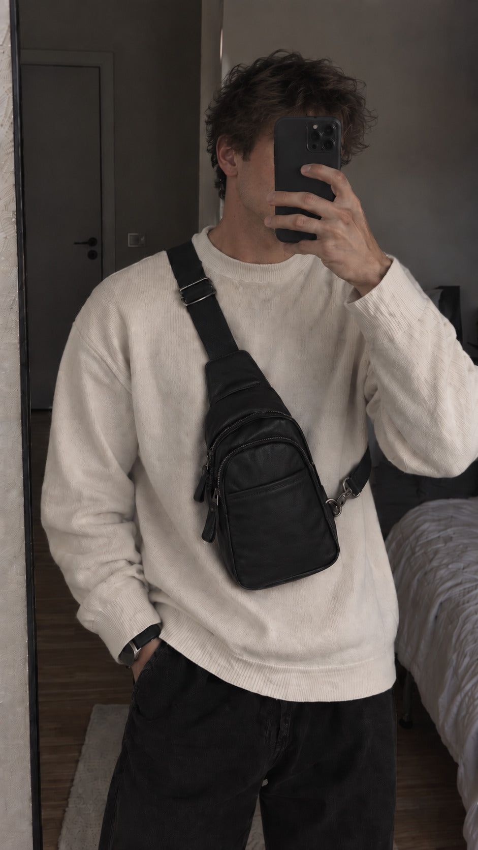 Man wearing a black sling crossbody bag with multiple zip compartments and adjustable strap