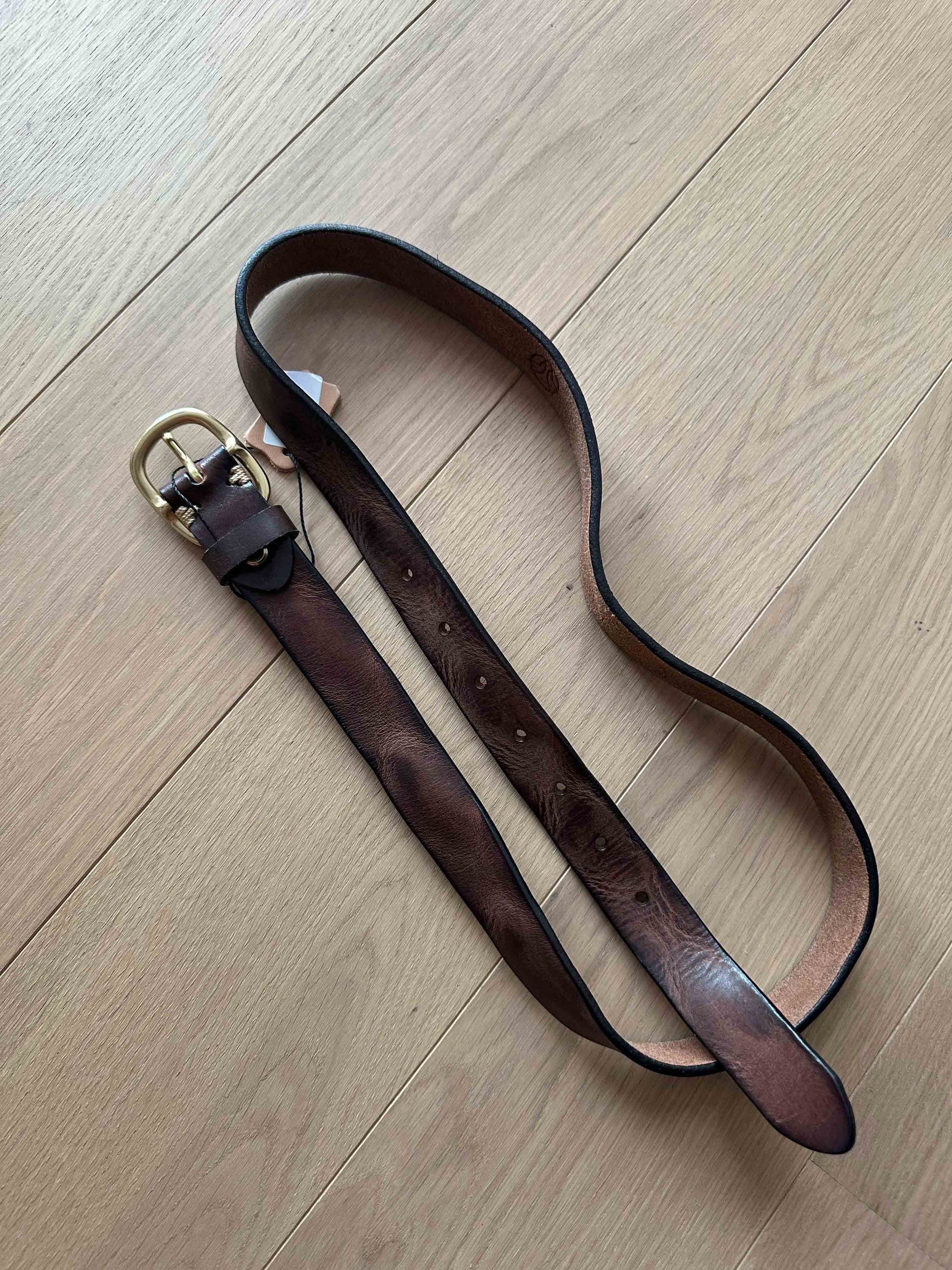 Brown leather belt with brass buckle on a light wooden floor