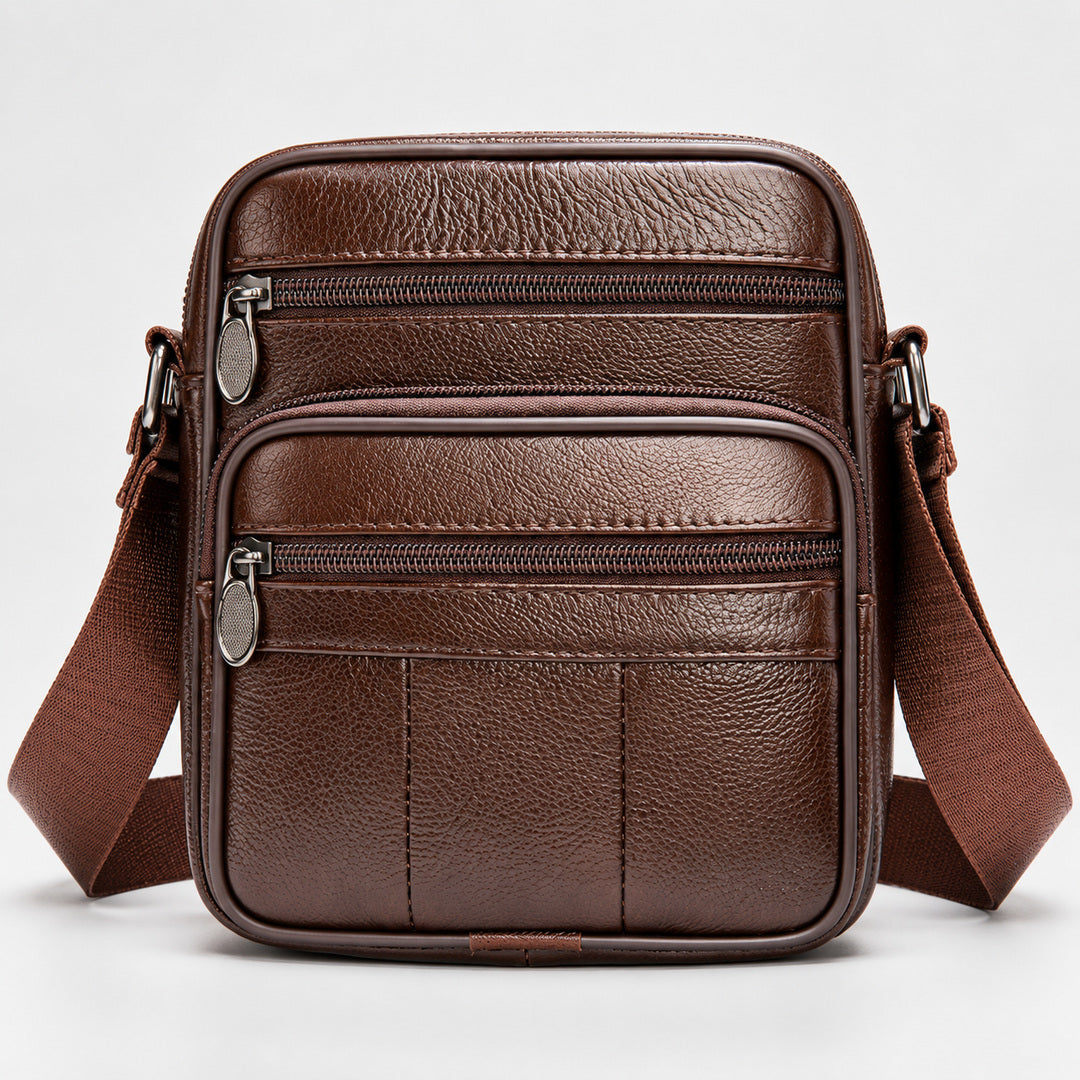 A brown leather crossbody bag with multiple zippered compartments and a wide adjustable shoulder strap, shown against a plain light gray background.