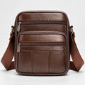A brown leather crossbody bag with multiple zippered compartments and a wide adjustable shoulder strap, shown against a plain light gray background.
