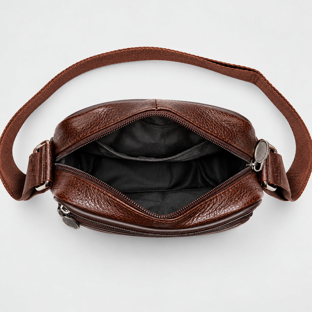 A brown textured leather crossbody bag shown open from a top-down view, displaying its black interior lining and adjustable strap on a light gray background.