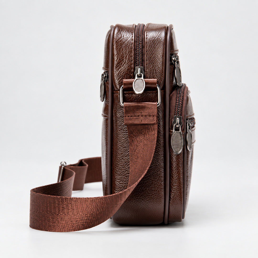 A brown textured leather crossbody bag with multiple zippered compartments and an adjustable woven strap, shown from a side profile view on a light gray background.
