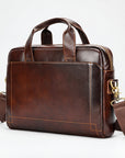 A dark brown leather briefcase with dual top handles, a detachable shoulder strap, and gold-tone hardware, photographed on a clean white studio background.