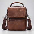 A brown textured leather crossbody bag with a top handle, front zip pocket, and matching shoulder strap, photographed against a light gray studio background.