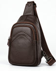 A dark brown textured leather sling bag with an adjustable shoulder strap, shown from a three-quarter angle on a white background.