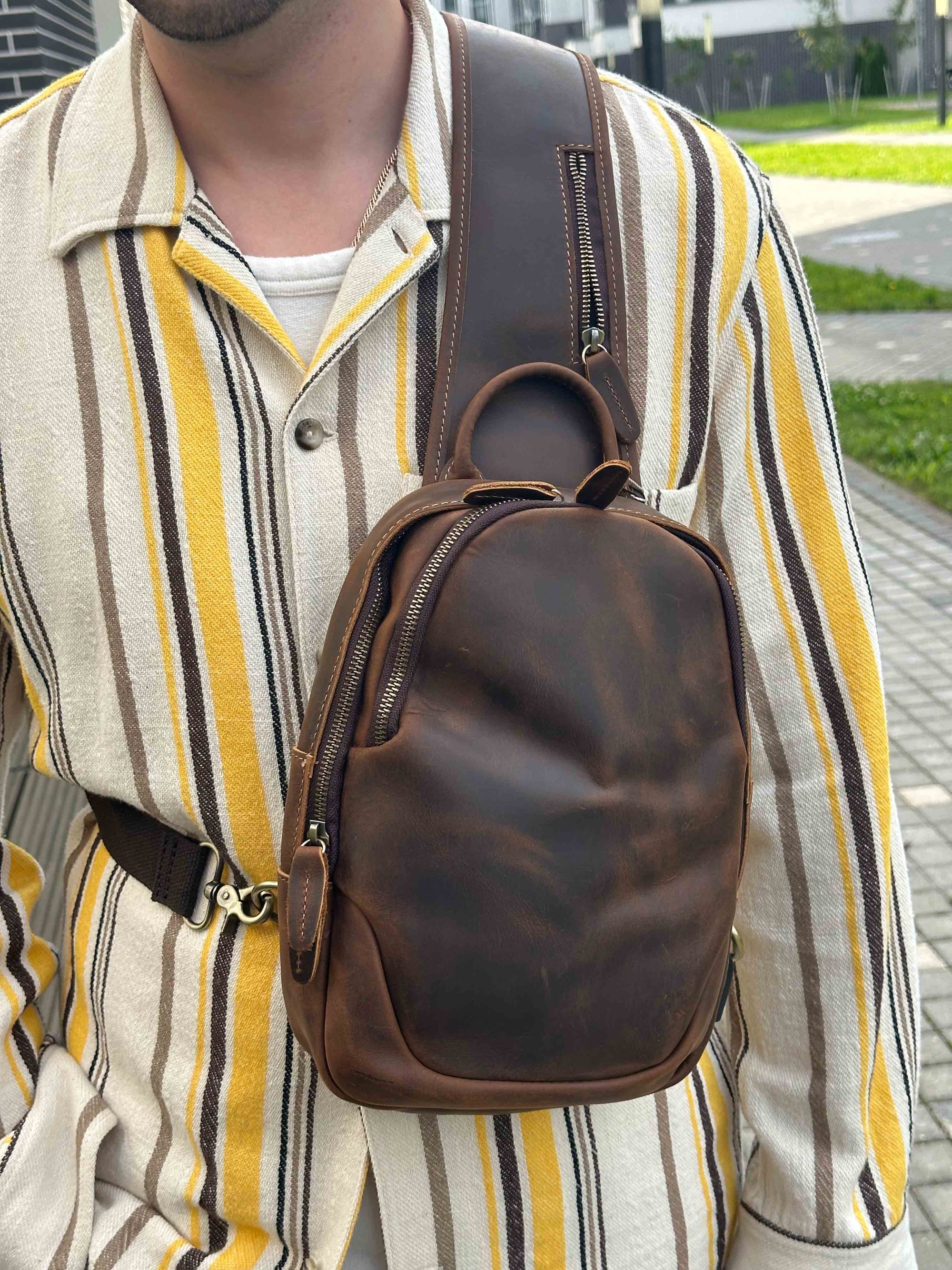 Person wearing a brown leather crossbody bag over their shoulder with a striped shirt.