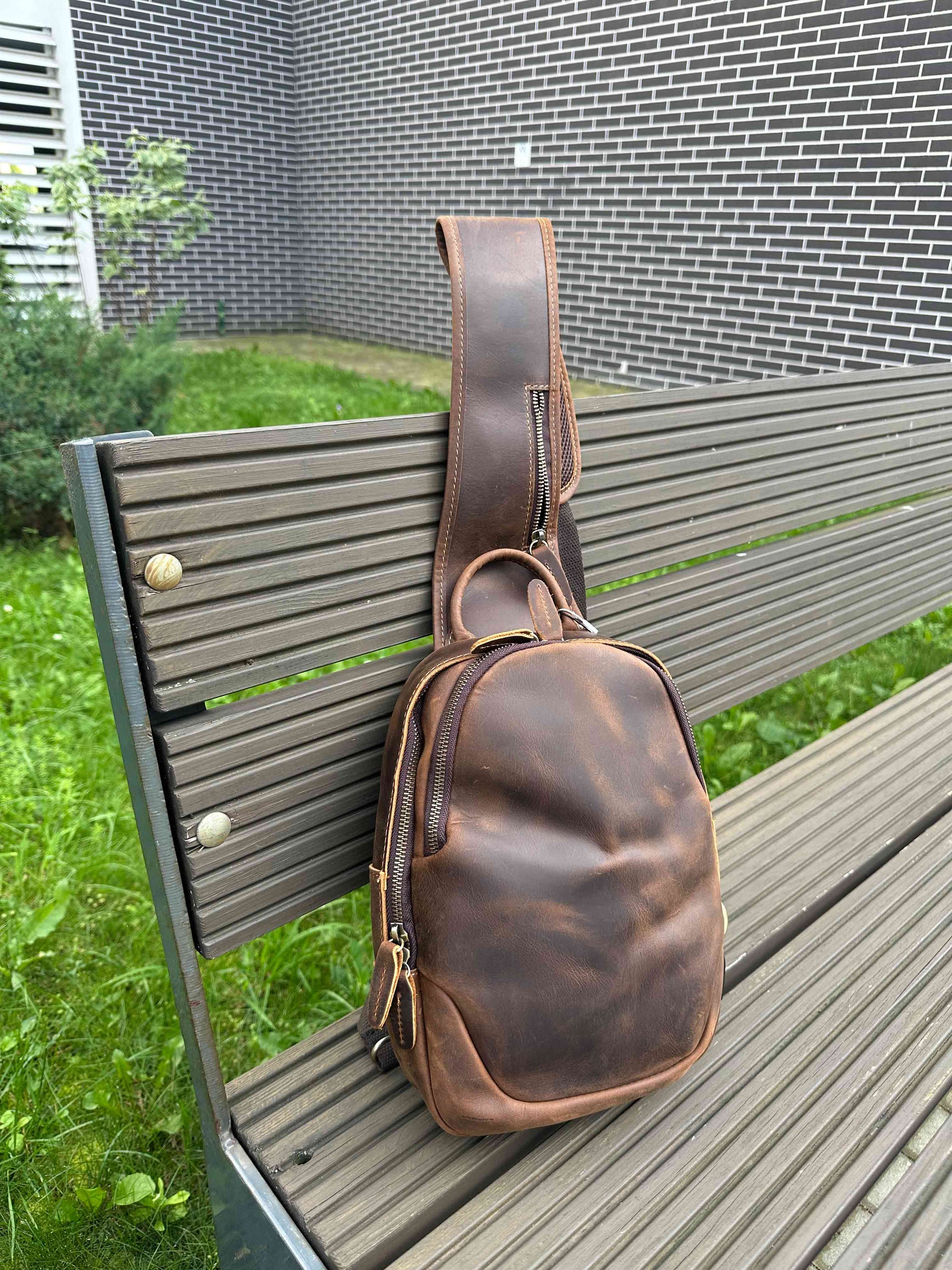 Brown leather crossbody bag on a wooden deck with grass in the background