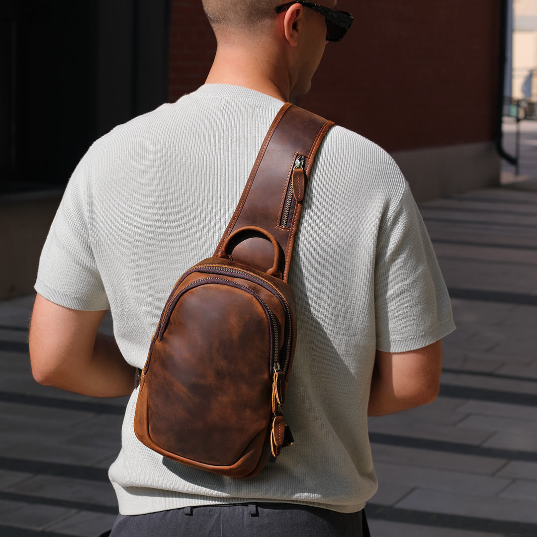 Men wearing a brown leather sling bag over his shoulder on a city street.