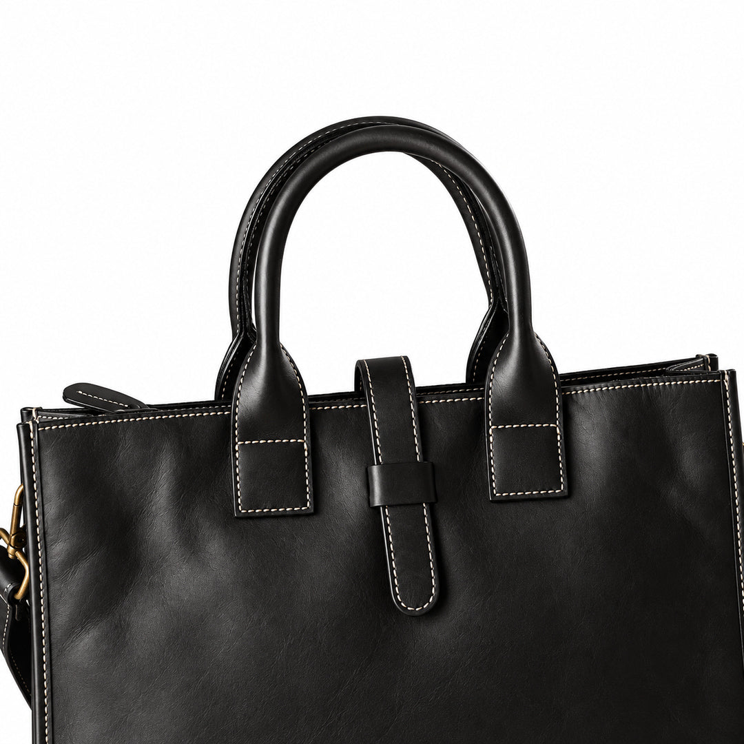 Men's black full-grain leather tote bag handle detail with contrast stitching and a central leather tab