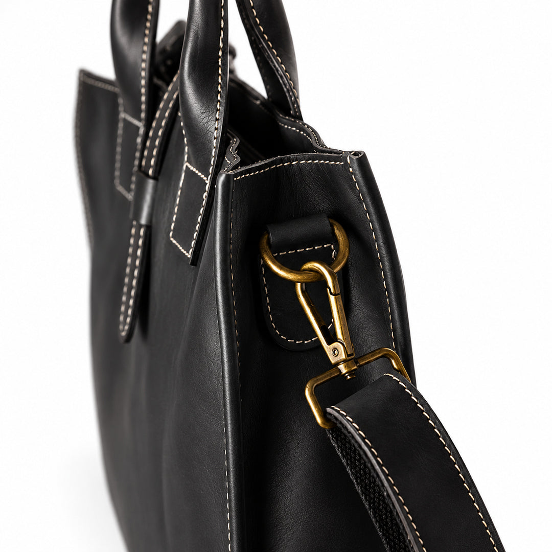 Men's black full-grain leather tote bag strap attachment with a gold-tone clasp and stitched leather tab