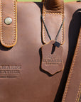 Men's leather work bag with Elwards Leather logo and detachable strap resting on a wooden surface in natural light.